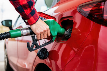 Person filling up a red car with gasoline at a gas station
