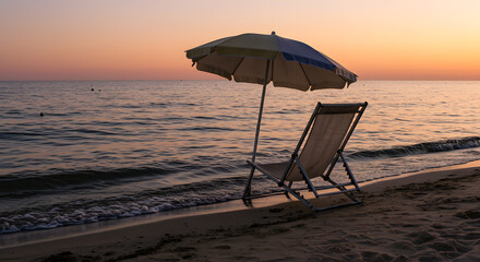 Sunset view of beach chair and umbrella facing ocean waves on quiet shoreline