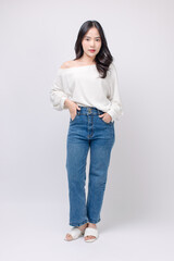 Full body portrait happy smile young asian beautiful woman curly hair wearing long sleeved shirt, blue jeans outfit, casual standing pose on white background joy positivity fashion lifestyle concept.