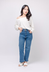 Full body portrait happy smile young asian beautiful woman curly hair wearing long sleeved shirt, blue jeans outfit, casual standing pose on white background joy positivity fashion lifestyle concept.