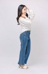 Full body portrait happy smile young asian beautiful woman curly hair wearing long sleeved shirt, blue jeans outfit, casual standing pose on white background joy positivity fashion lifestyle concept.