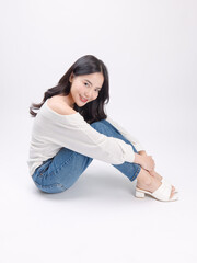 Portrait happy smile young asian beautiful woman curly hair wearing long sleeved shirt, blue jeans outfit, casual relax on floor in studio, sitting on white background joy positivity fashion concept.