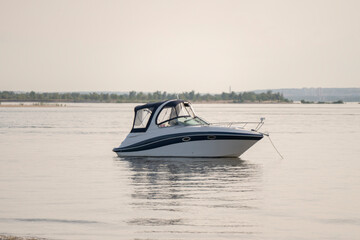 Motor boat anchored near sandy beach at calm waters during late afternoon
