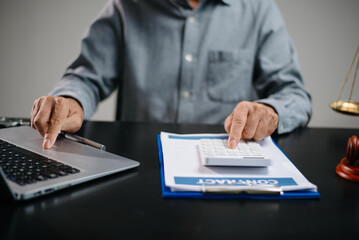 businessman reviews legal contract with calculator and laptop in office. Concept of finance, law,...