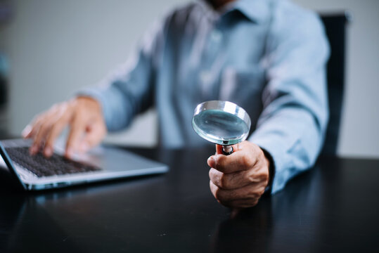 man using magnifying glass while working on laptop. Concept of research, investigation, security analysis, attention