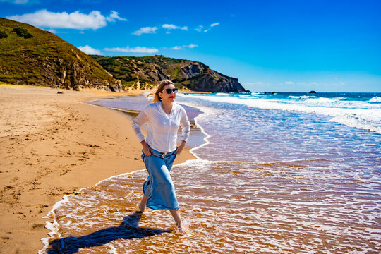Portrait of beautiful middle aged woman enjoying walk on sandy beach in summertime. Front view. Amado beach on Algarve coast in Portugal	