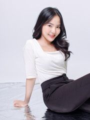 Portrait cheerful young asian beautiful woman curly hair wearing long sleeved shirt, black long pants outfit casual relax on floor in studio laydown on white background joy positivity fashion concept