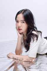 Portrait cheerful young asian beautiful woman curly hair wearing long sleeved shirt, black long pants outfit casual relax on floor in studio laydown on white background joy positivity fashion concept