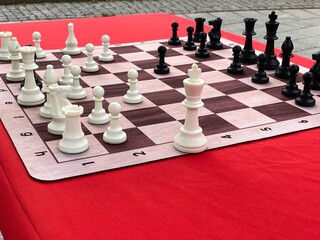Outdoor chessboard setup with white and black chess pieces on red table background