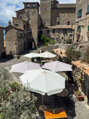 Tuscan old town view with stone buildings and outdoor restaurant with white umbrellas 
