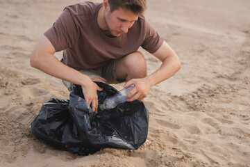 Man collects trash in a black bag while cleaning a sandy outdoor area