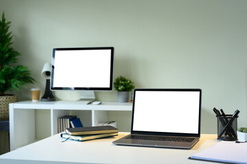 Modern office desk with laptop and desktop monitor, both featuring blank white screens