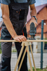Man cutting wooden plank with electric jigsaw at home backyard. Outdoor carpentry and DIY work