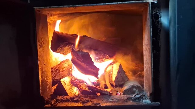 Crackling fire in a wood-fired sauna, showing glowing logs burning intensely and radiating warmth in the dim sauna interior.
