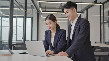 A couple sitting together looking at a laptop, possibly discussing work or planning their day