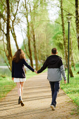 Fototapeta premium couple walking through scenic forest path, holding hands and embracing nature. springtime adventure in lush greenery evokes romantic connection and outdoor relaxation for lifestyle inspiration