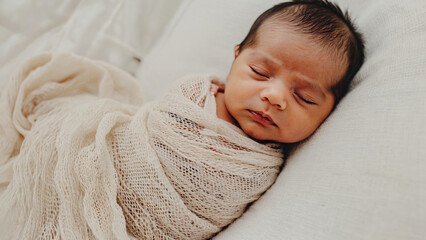 A newborn baby is wrapped in a soft blanket and lying peacefully on a bed