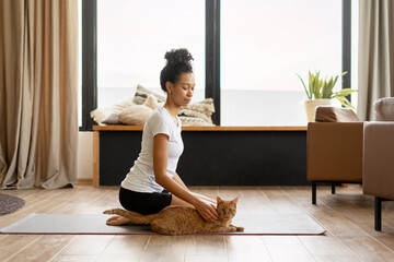Young woman practicing yoga with her ginger cat in the living room