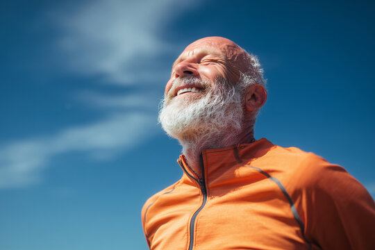 A man with a white beard and a red shirt is smiling and looking up at the sky. The sky is blue and clear, and there are no clouds in the sky. The man is enjoying the beautiful day and the clear sky