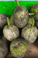 Close-up of fresh breadfruits with rough, green-brown textured skin displayed at a traditional market, stacked together for sale in a natural setting.