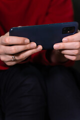 Woman wearing a vibrant red sweater and dark pants holds a smartphone horizontally in both hands, sitting on the toilet. Vertical photo