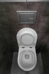 Modern bathroom interior featuring a pristine white toilet bowl against a backdrop of dark gray tiled walls, creating a stylish and contrasting aesthetic. Vertical photo