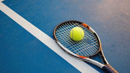 A tennis racket and ball sit on a tennis court, ready for play