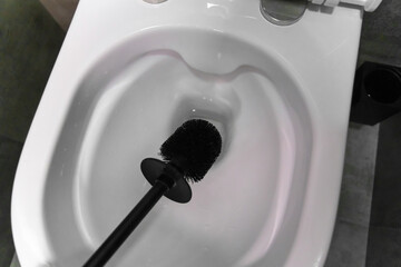 Modern black toilet brush hovering over an open white toilet bowl, preparing for cleaning in a contemporary bathroom featuring a stylish gray tiled floor