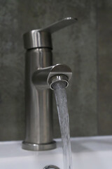 Clean water flowing from a brushed nickel faucet in a bathroom creates a refreshing atmosphere, emphasizing hygiene and promoting a sense of purity and wellness in the space. Vertical photo