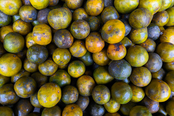 A pile of ripe local oranges with natural blemishes and varied colors, displayed at a traditional...