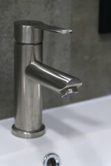 Close-up view of a sleek, modern stainless steel faucet positioned above a white ceramic sink, showcasing contemporary bathroom design and fixtures. Vertical photo