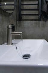 Close-up view of a modern bathroom sink featuring a stainless steel faucet, white ceramic basin, and a textured concrete wall, creating a stylish and minimalist atmosphere. Vertical photo