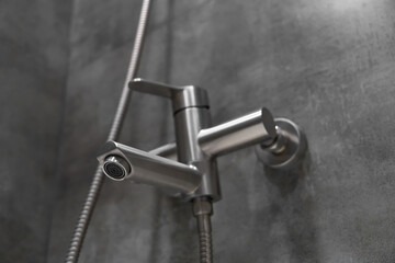 Modern shower faucet with flexible hose is mounted on grey tiled wall in contemporary bathroom, offering convenient and stylish water control for refreshing shower experience