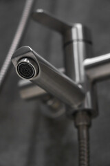 Close-up of a contemporary chrome faucet spout, showcasing its sleek design and highlighting the aerator, ready to deliver water in a bathroom setting. Vertical photo