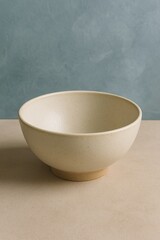 A simple ceramic bowl is placed on a neutral background, demonstrating minimalist design. The bowl is designed with a neutral color and its surface is smooth.