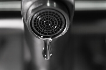 Close-up view of water dripping from a faucet spout, emphasizing the importance of water conservation and the need for reducing waste in both kitchen and bathroom settings