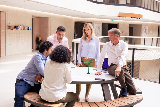 Multiracial business colleagues discussing ideas over wind turbine model in corridor