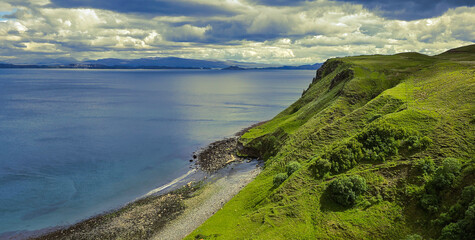Vibrant green cliffs descend toward a tranquil ocean, featuring dramatic skies and highlighting the...