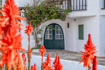 Vivid Red Flowers Framing Arched Green Door in Binibeca Vell. Menorcan Whitewashed Architecture, Coastal Village Charm, Bright Summer Day