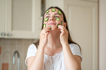 Woman with cucumber slices on her face enjoying a healthy skincare routine in a bright kitchen