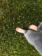 Barefoot woman walking on lush green grass with small white flowers, enjoying nature and feeling of earth beneath their feet in serene outdoor environment after rain
