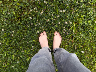 Barefoot woman standing on lush green grass with small white flowers, enjoying nature and the feeling of earth beneath their feet in a serene outdoor environment after rain