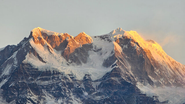 Majestic, snow-clad peaks of a Himalayan mountain range bathed in the warm, golden light of sunrise or sunset, highlighting their rugged beauty and towering presence.