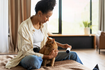 Woman using lint roller while holding ginger cat on bed