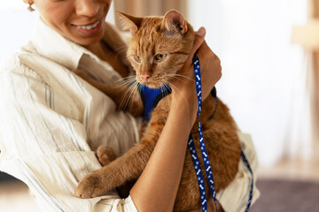 Woman holding ginger cat wearing harness and leash