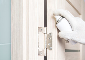 close up of door hinge being lubricated with silicone from a pressure can
