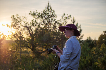 Young Caucasian woman holds camera during golden hour in nature