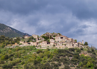 Fototapeta premium Timeless Aristot village clings to Pyrenean hillside beneath brooding clouds