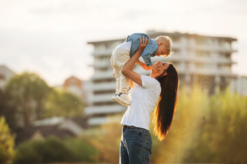 Up in the air, holding boy in hands. Mother and son are together on the summer field