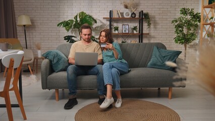 Couple Shopping Online Using Laptop on Comfortable Sofa